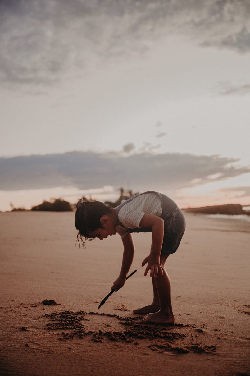 Little Girl Writing on the Sand with a Stick